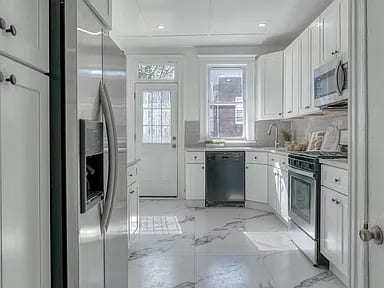 Bright renovated kitchen with white cabinetry, stainless steel appliances and marble-look flooring